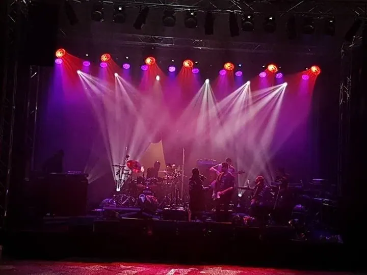 Palco di un concerto con luci viola e fasci bianchi