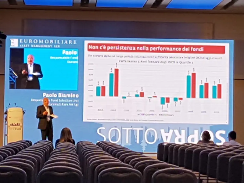 Relatore sul palco davanti a un LED wall con un grafico