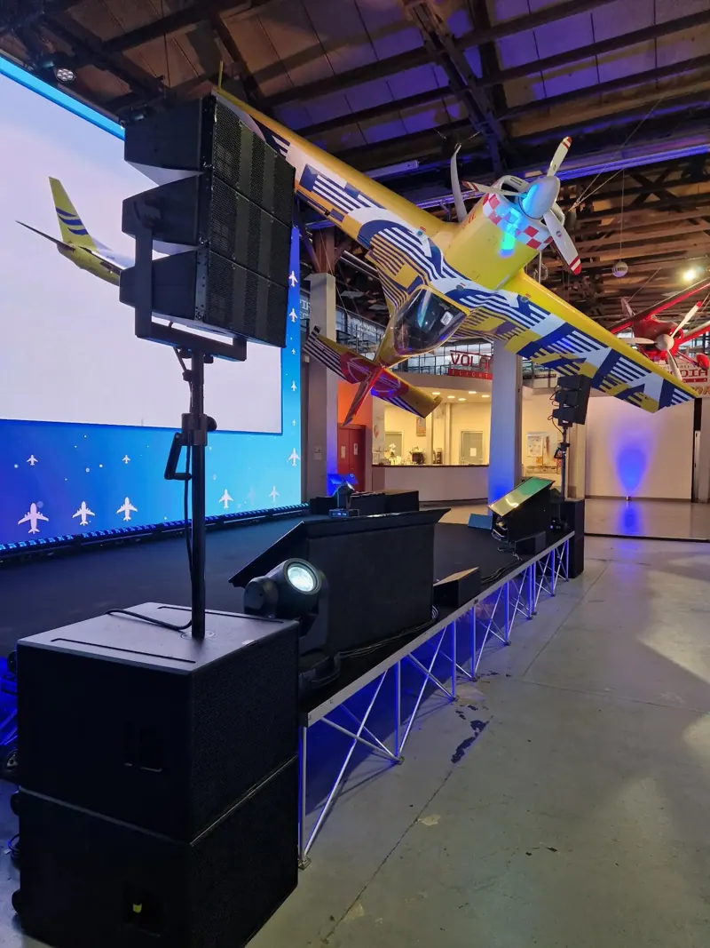 Palco con truss, casse e un aereo d'epoca sopra la sala